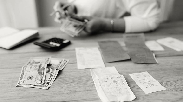 Hands counting banknotes over a desk of receipts and a calculator.